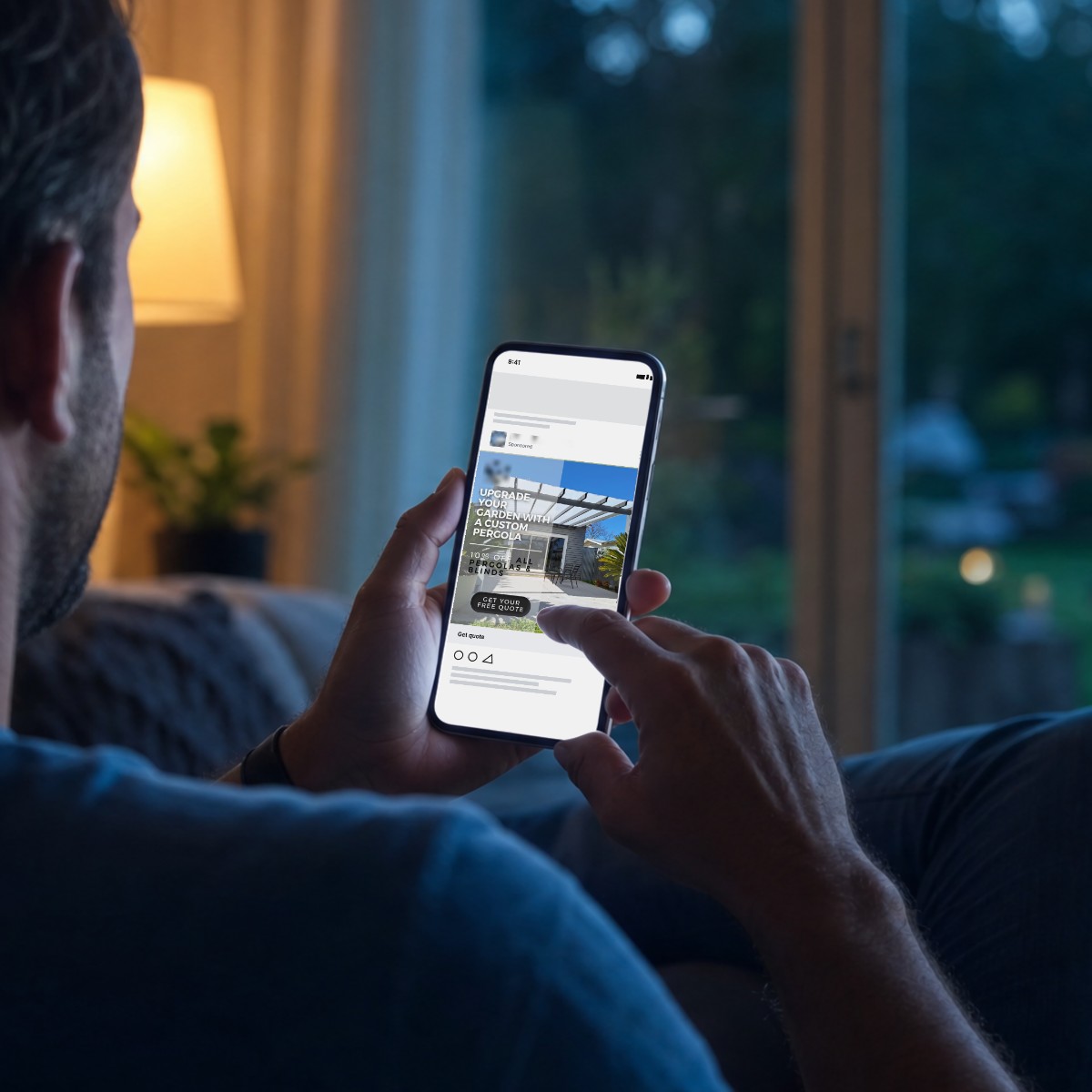 Homeowner on the sofa at dusk scrolling a social feed on their phone, showing a sponsored pergola ad from one of our clients